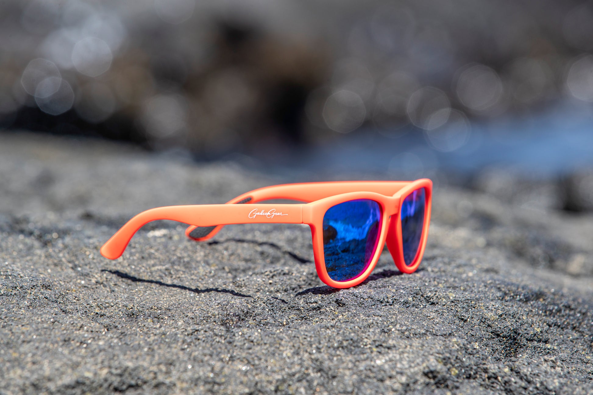 Orange sunglasses with blue lenses on a black sand beach