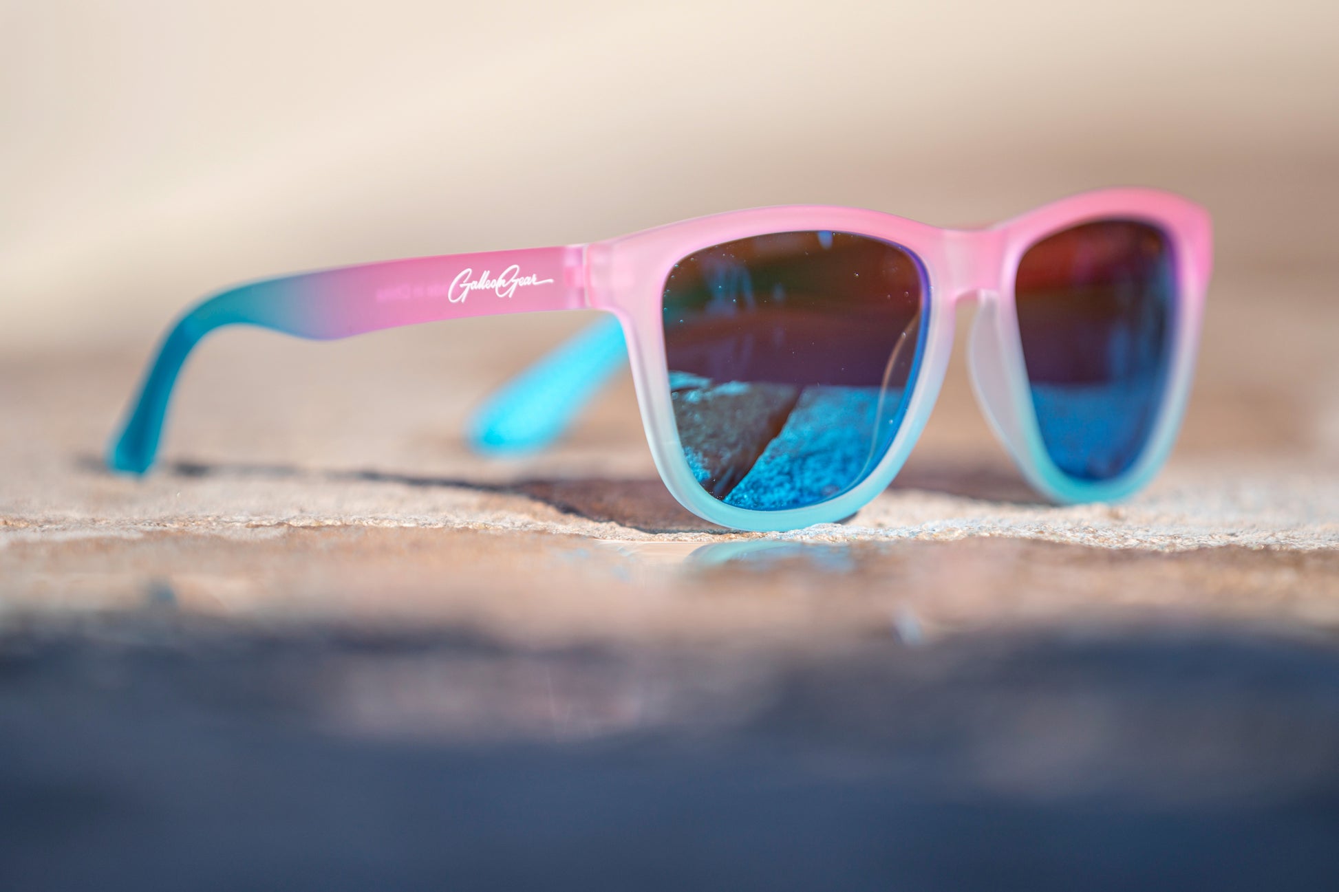 Pink and blue gradient sunglasses with blue lenses on a concrete.