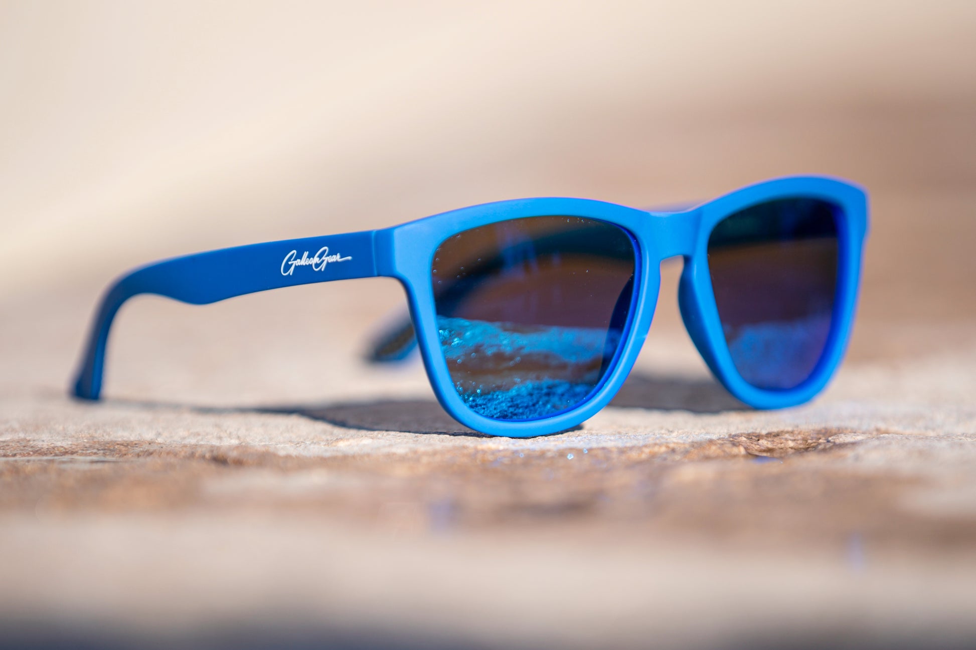 Blue sunglasses with a brand logo on a concrete surface.