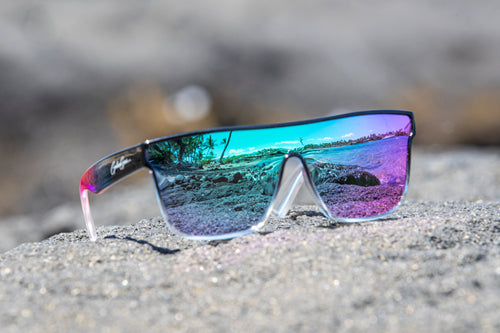 Sunglasses with reflective purple and blue/green lenses on a black sandy surface