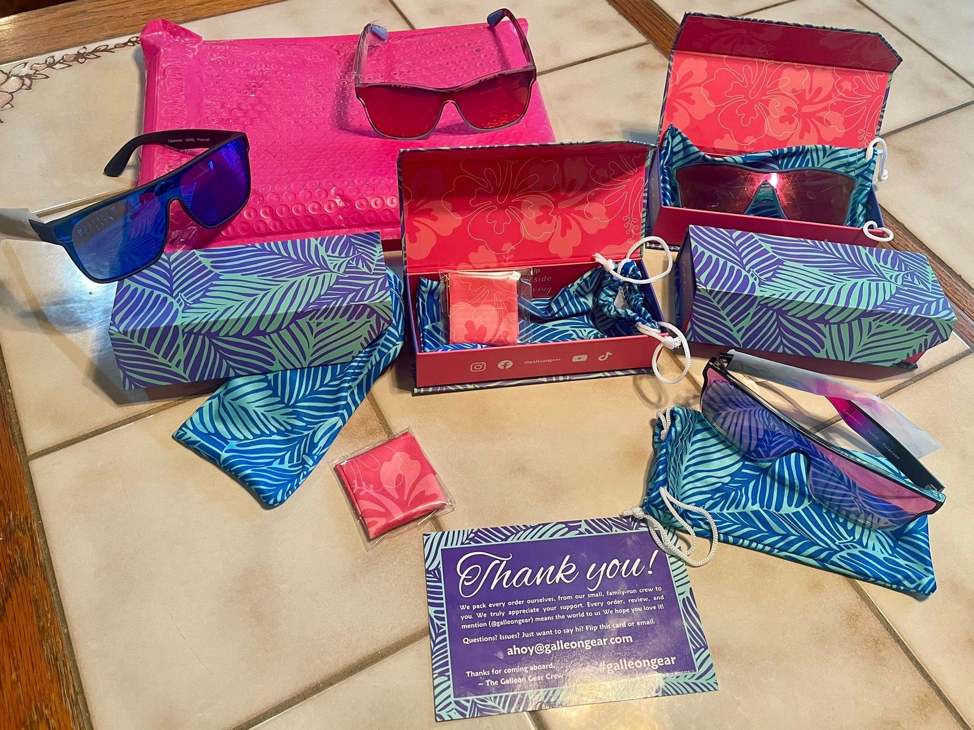 Collection of colorful sunglasses and cases on a tiled floor with a 'Thank you' card.