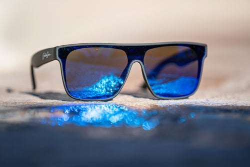 Black sunglasses sunglasses with blue reflective lenses reflecting sunlight off of a wet stone surface.