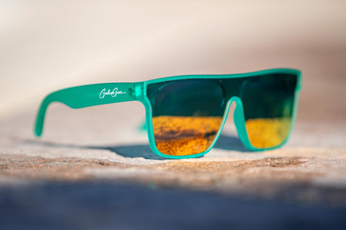 A bright colored sea foam green that is slightly transparent sunglasses with golden orange reflective lenses on a stone surface