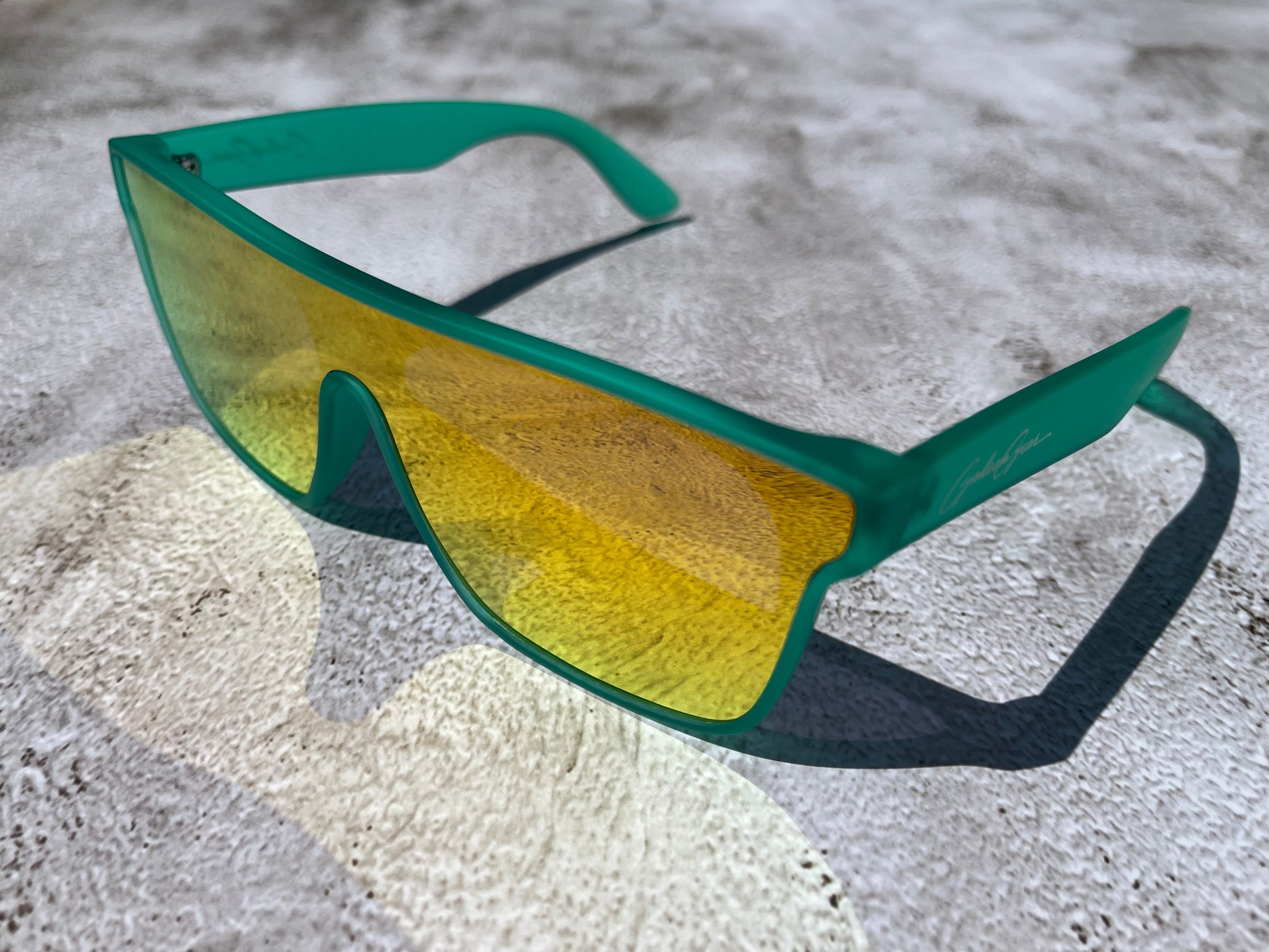 A slightly transparent seafoam green frame with lenses that reflect back golden and orange on a textured surface.