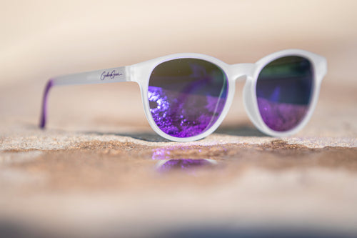 White slightly transparent framed sunglasses with purple lenses on a stone surface