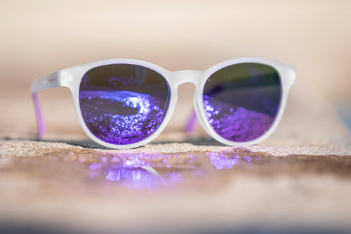 White semi-transparent sunglasses with purple-tinted lenses on reflecting sunlight off of a puddle.