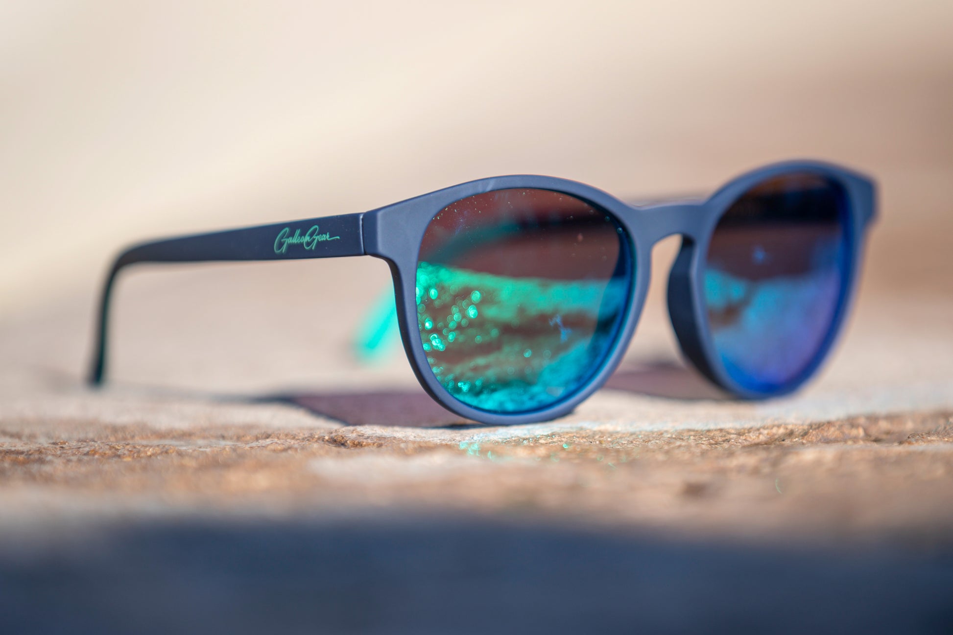 Navy blue sunglasses with blue and green reflective lenses on a concrete surface.