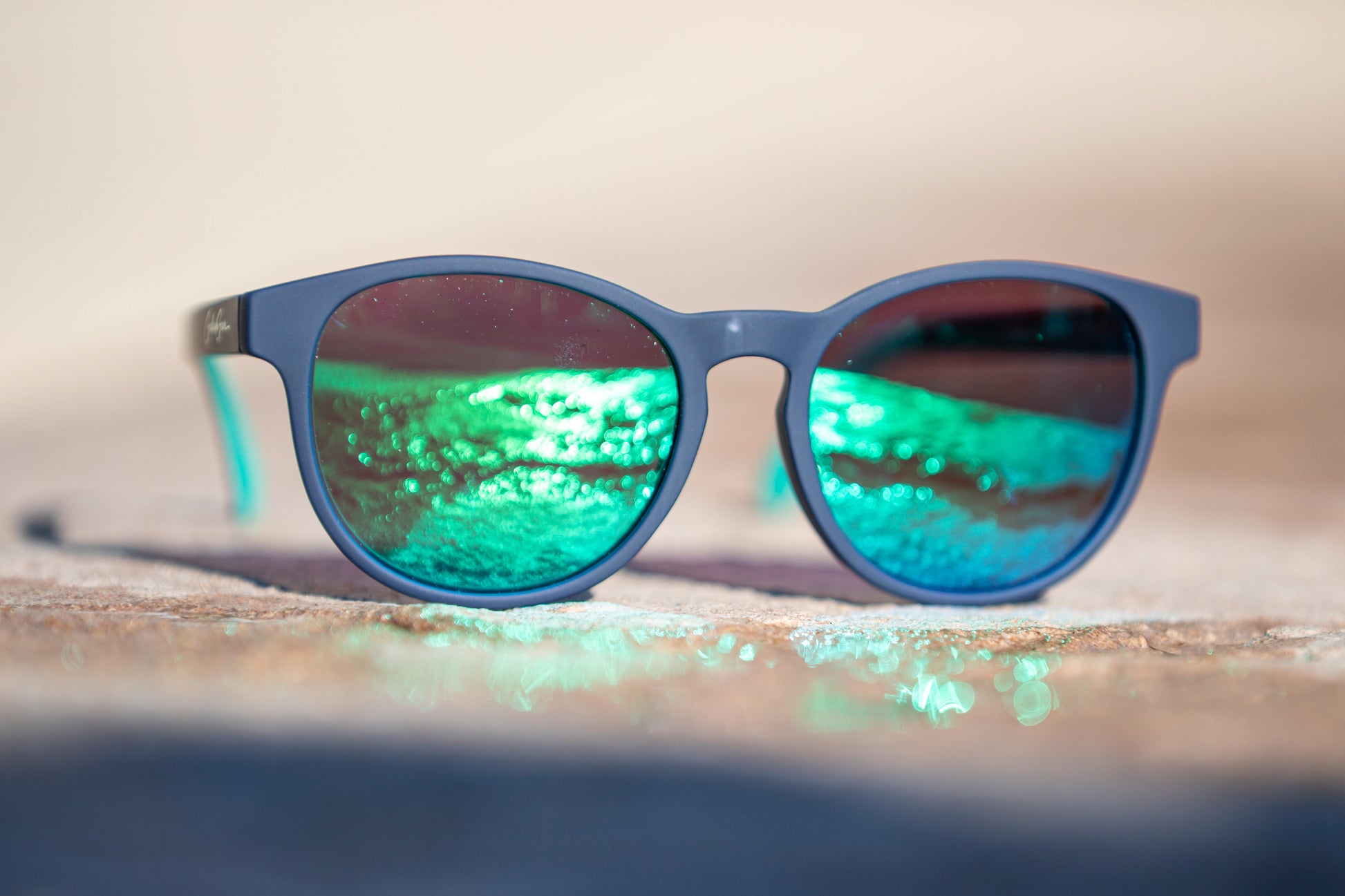 Navy blue sunglasses with green reflective lenses on a blurred stone background