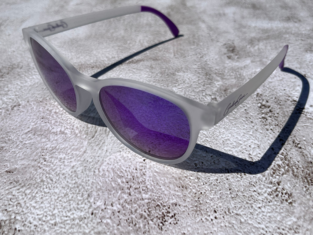 White semi transparent sunglasses with purple reflective lenses on a textured surface