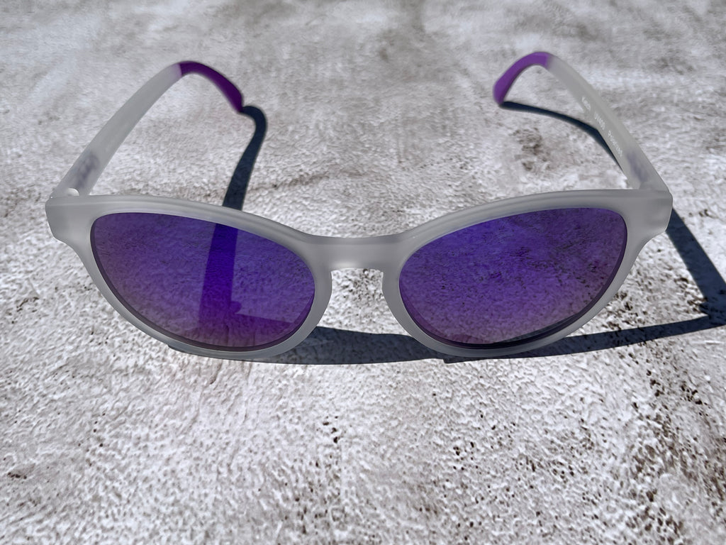 Sunglasses with purple lenses and white semi transparent frame on a textured surface
