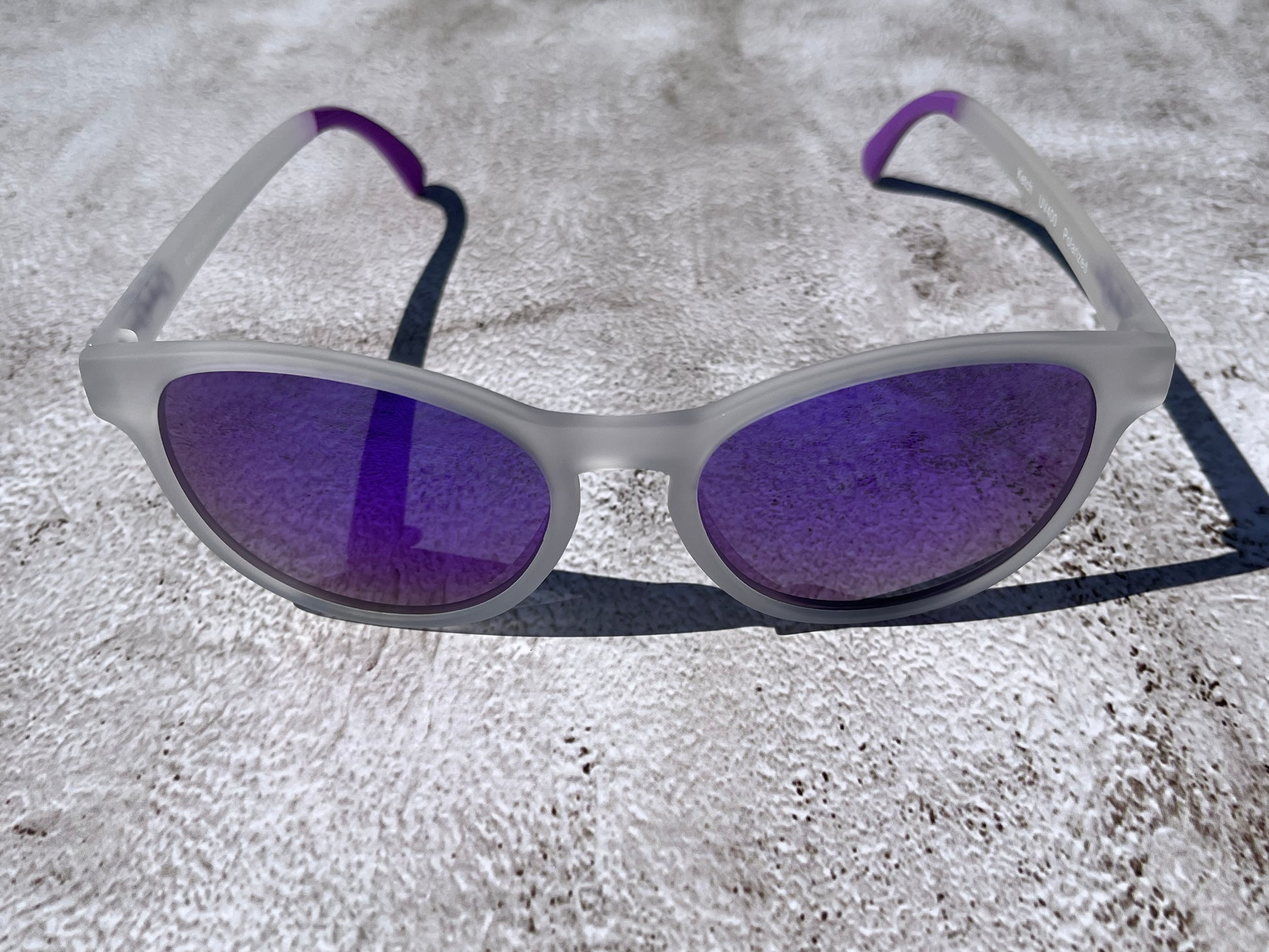 Sunglasses with purple lenses and white semi transparent frame on a textured surface