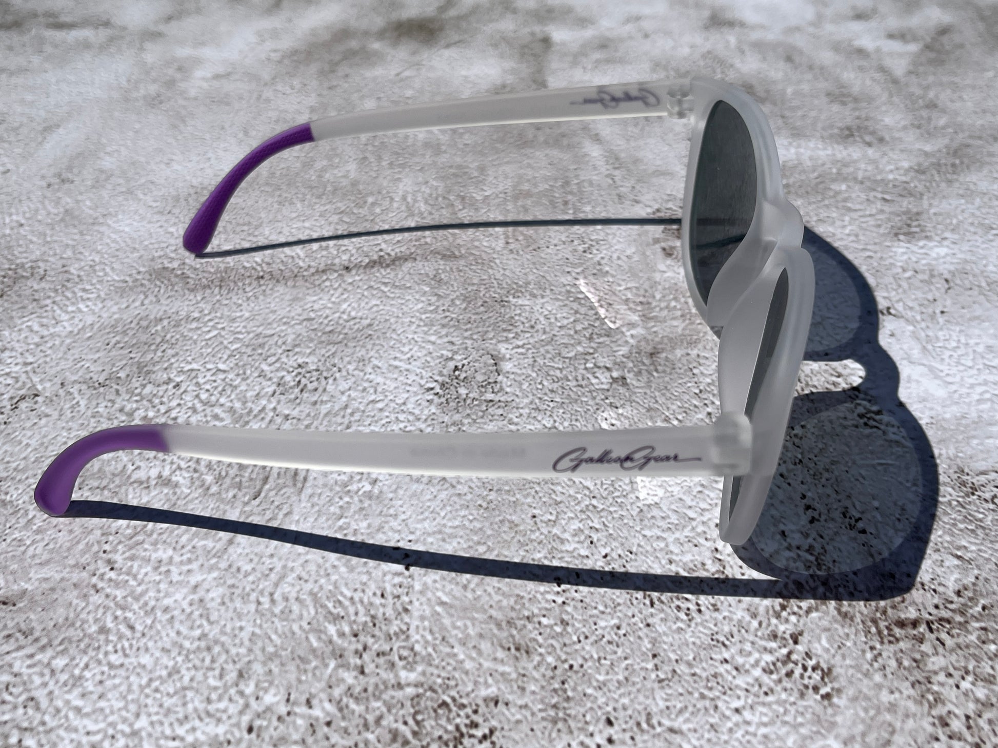 Sunglasses with purple temple grips on a textured surface