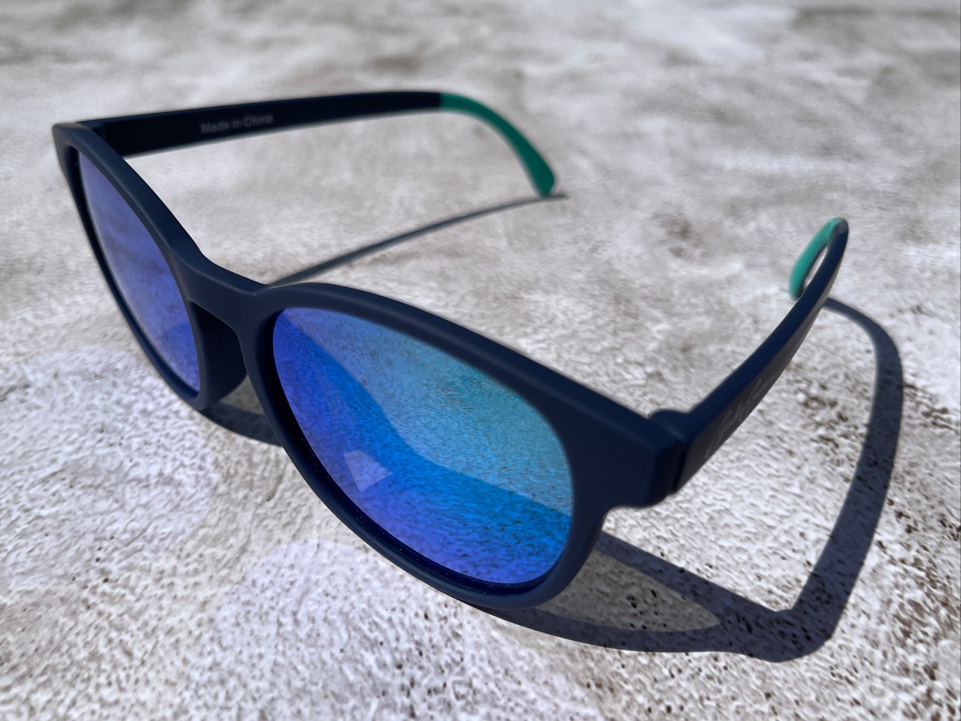 Navy blue sunglasses with blue reflective lenses on a textured surface