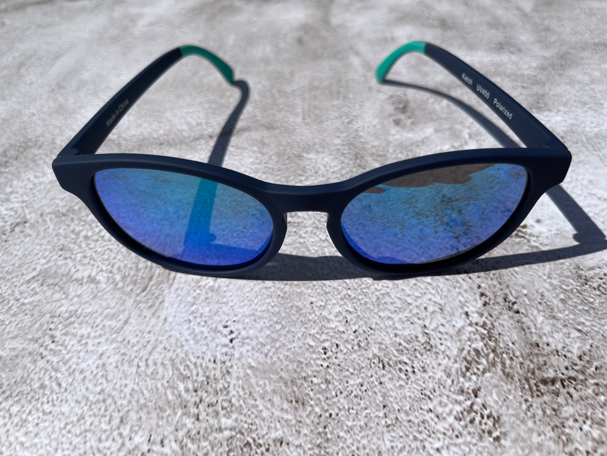 Navy blue sunglasses with blue lenses on a textured surface