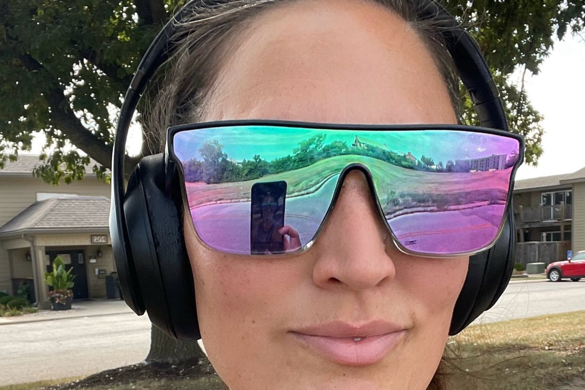 Person wearing large reflective sunglasses and headphones outdoors.