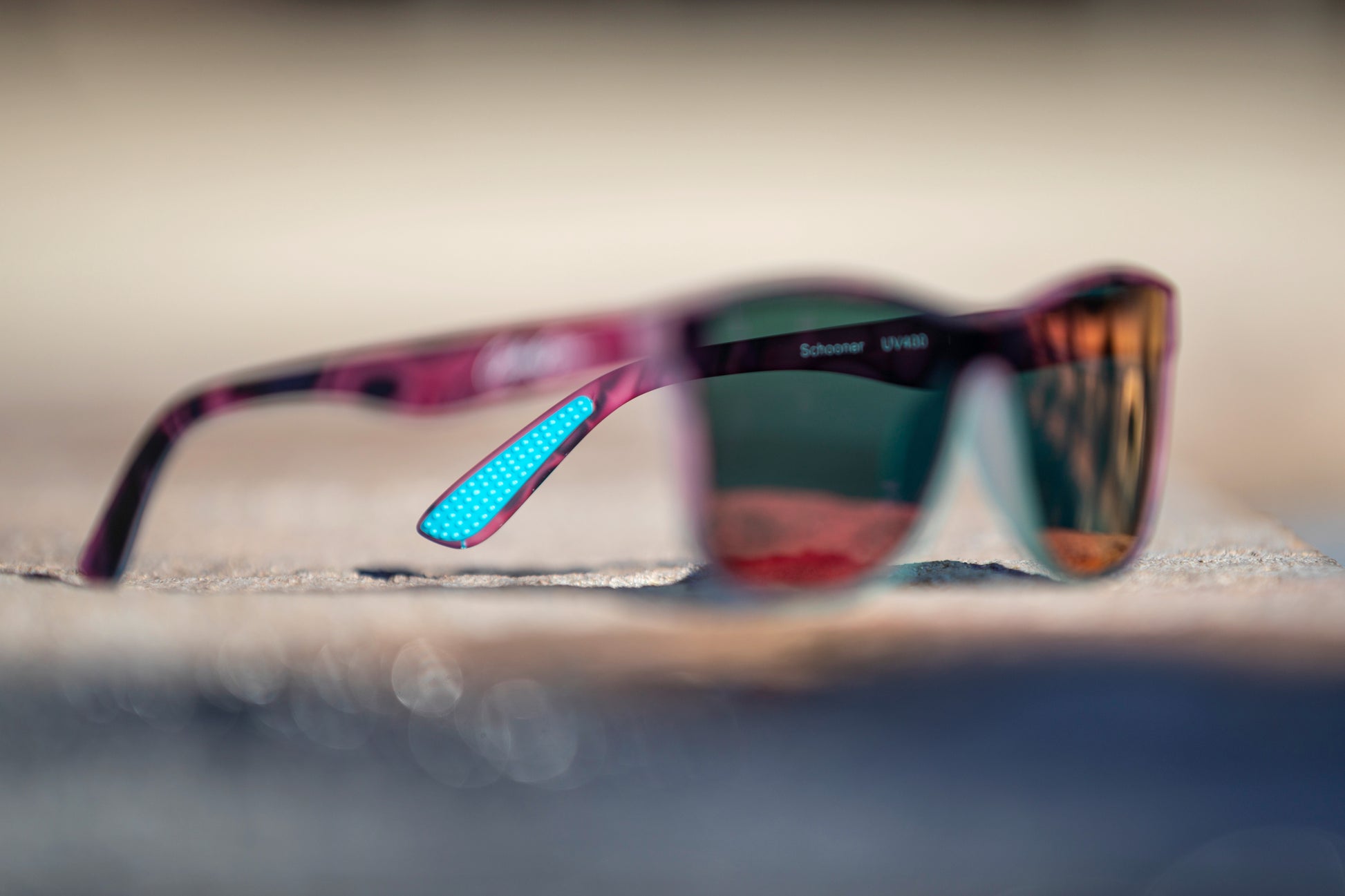 Blurred pink and black sunglasses on a blurred background with a focus on the turquoise temple grips.