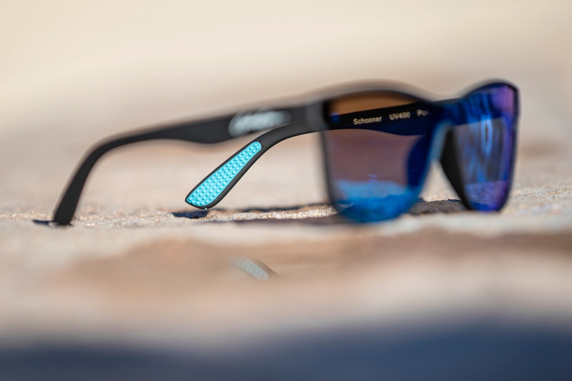 Blurred black sunglasses with blue lenses on a blurred background with the focus on the light blue temple grips.