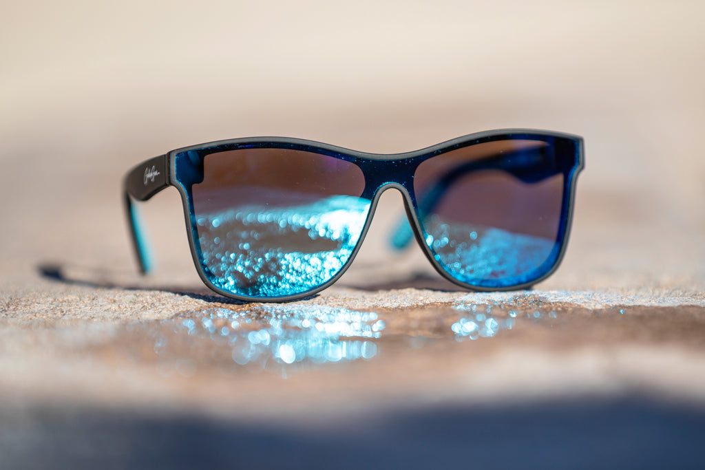 Black Sunglasses with a light blue reflection on the lenses of sunlight off of a puddle on a blurred stone surface.