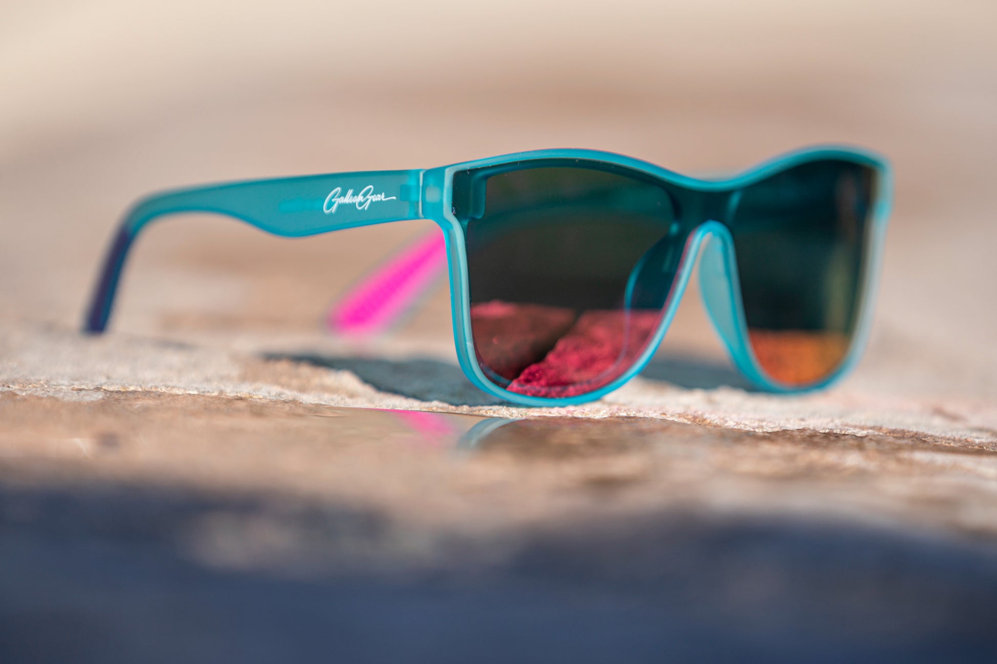 Light aqua blue sunglasses with orange and pink reflective lenses with a blurred background.