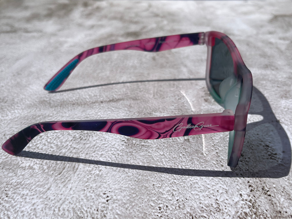 Sunglasses with a pink and black frame on a textured surface
