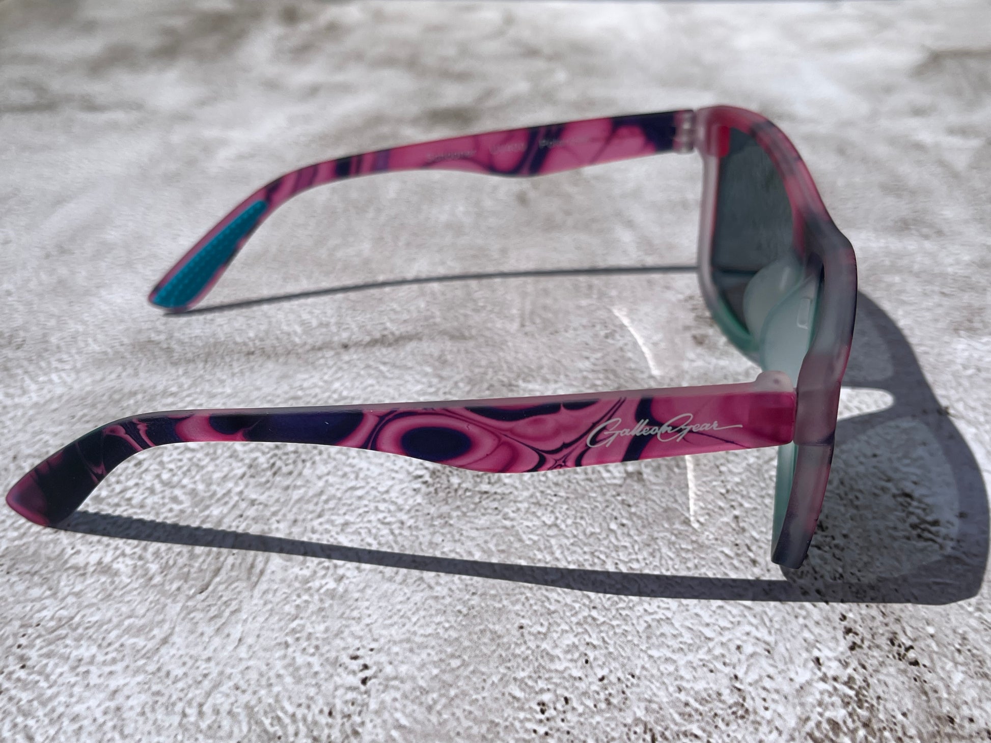 Sunglasses with a pink and black frame on a textured surface
