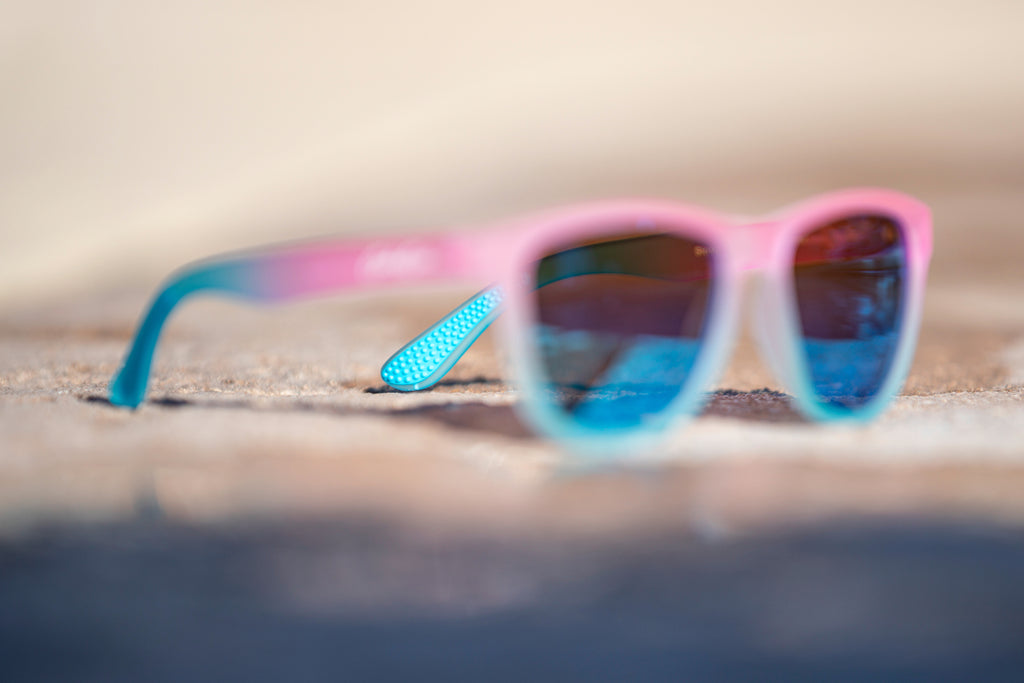Blurred pink and blue gradient sunglasses with blue lenses, with a focus on the detail of the light blue temple grip. 