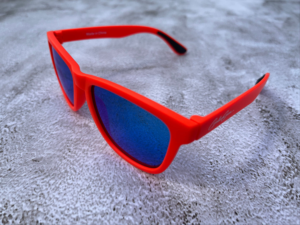 Bright orange sunglasses with blue lenses on a textured surface