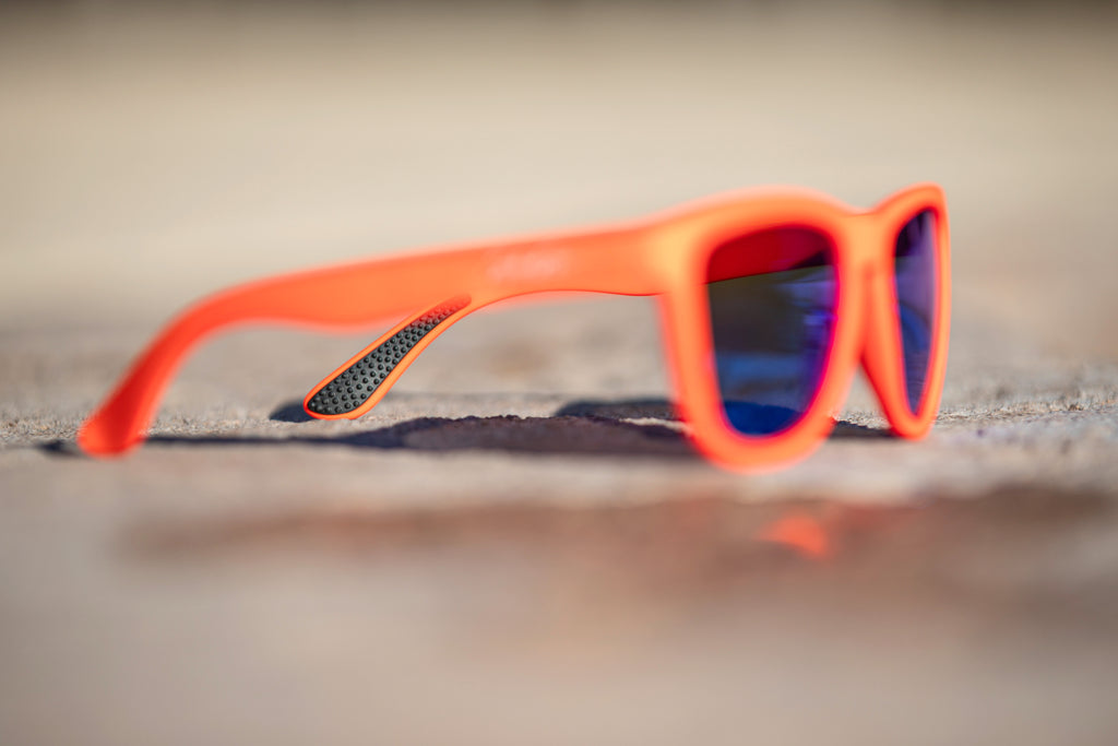 Blurred orange sunglasses with blue lenses on a blurred background, where the only focus is on the black temple grip of the sunglasses.
