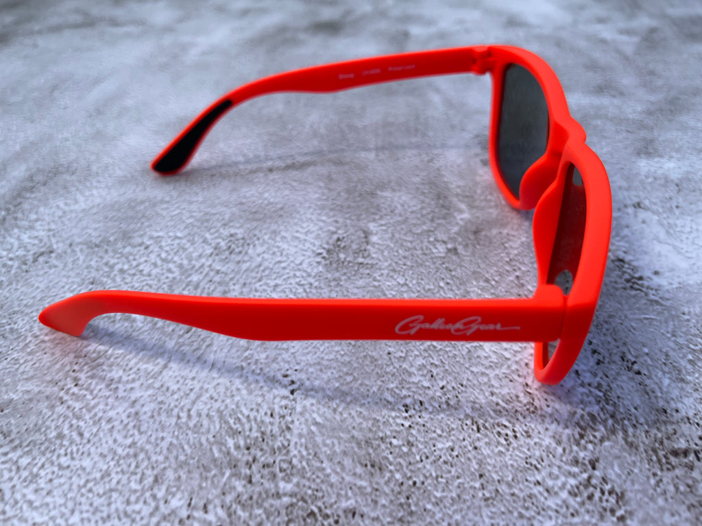 Bright orange sunglasses with a brand logo on a textured gray surface