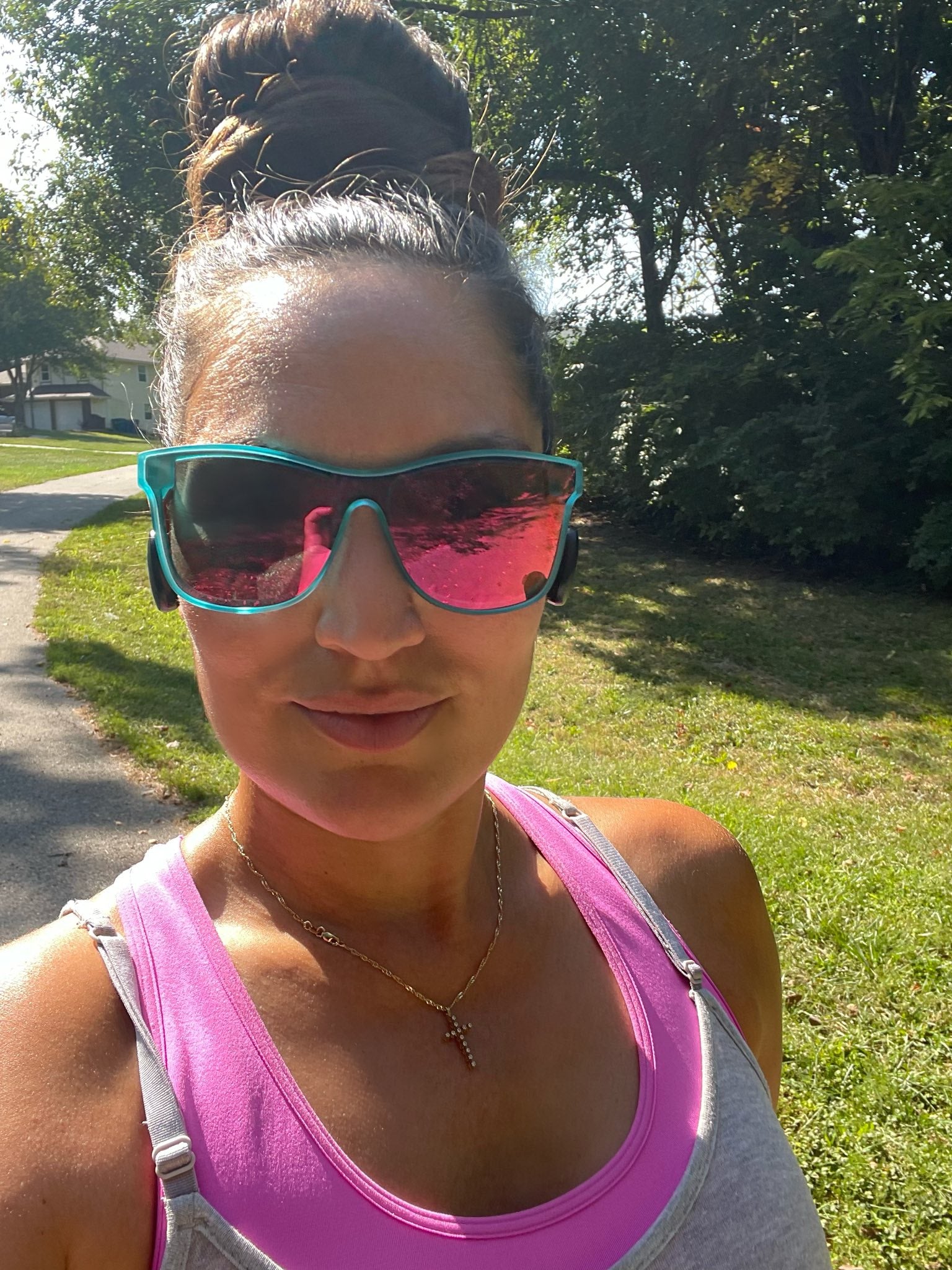 Woman wearing sunglasses on a walking path with trees and grass behind her.